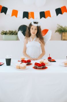 A girl in an angel costume celebrates with cupcakes at a festive Halloween-themed party.