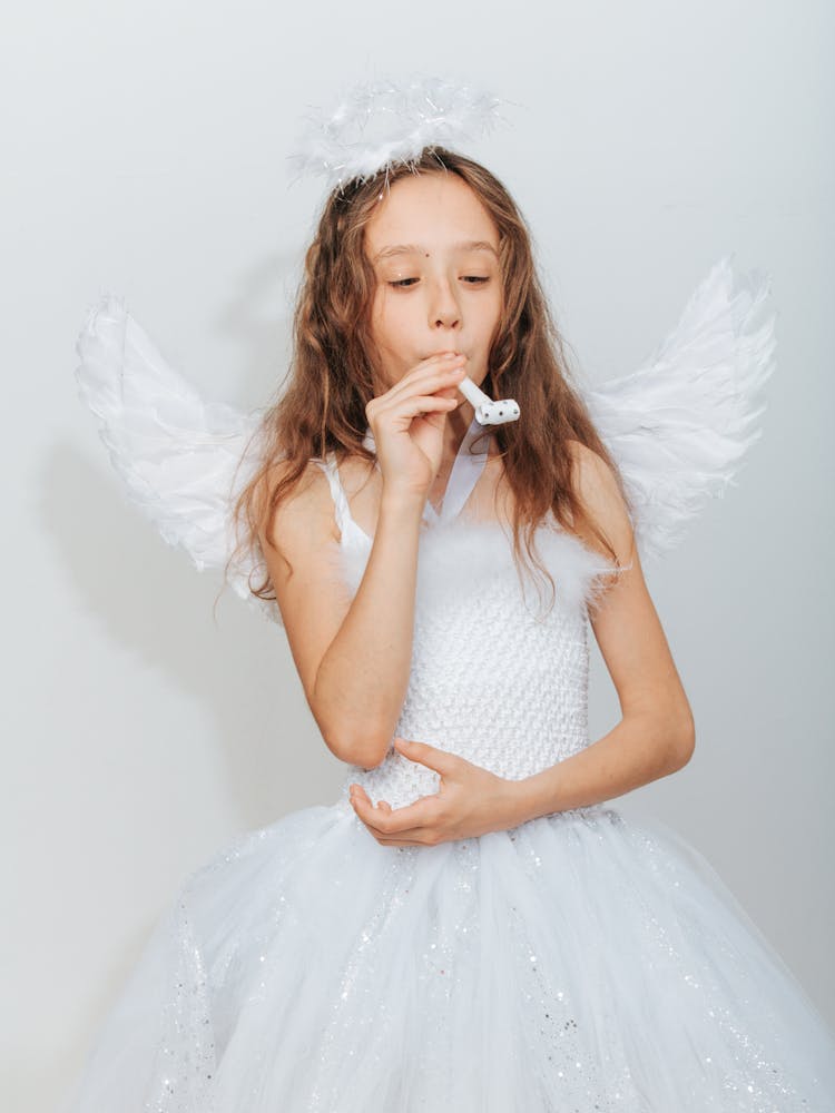 Cute Girl In Angel Costume Blowing A Party Horn