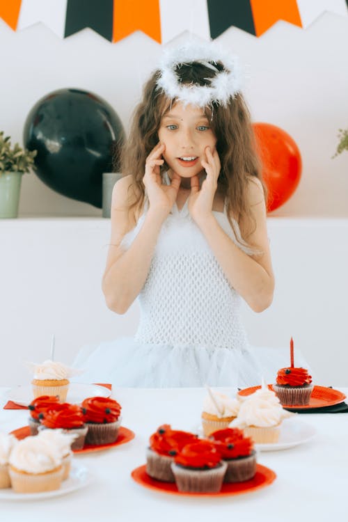 Free Girl in Angel Costume Looking Surprised at the Cupcakes Stock Photo