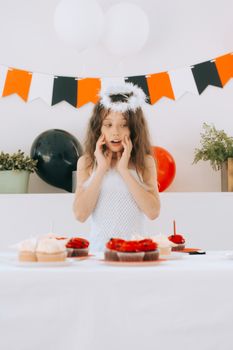 Girl dressed as angel celebrates with cupcakes at a festive party.