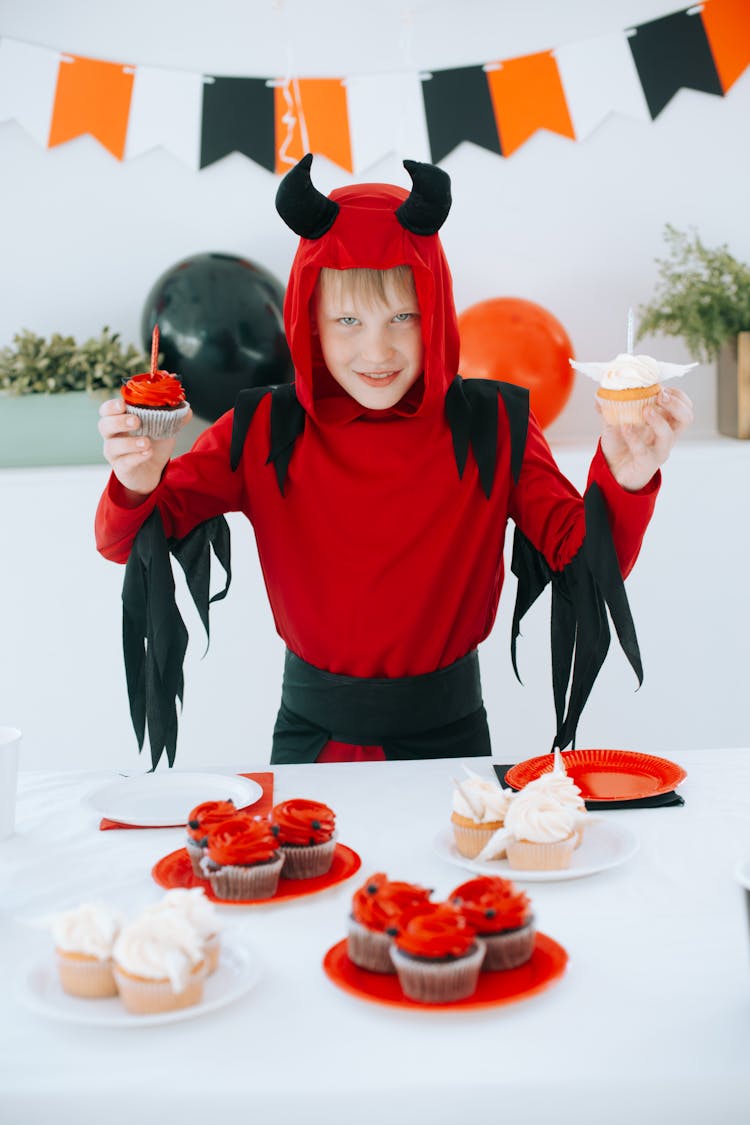 A Scary Boy In Devil Costume Holding Cupcakes