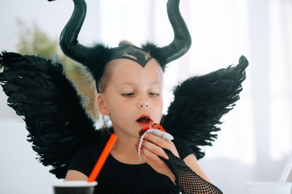Child dressed as Maleficent enjoying a cupcake during Halloween.