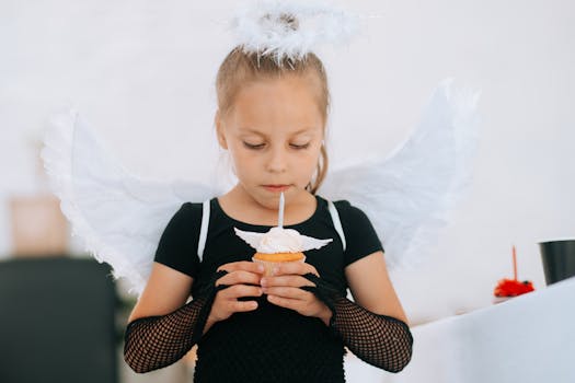 A young girl dressed as an angel with wings and halo holding a cupcake at a party.