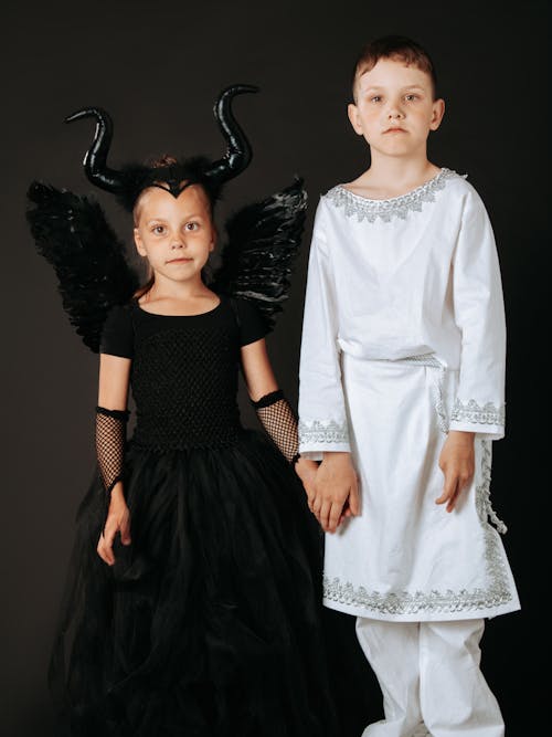 A Young Boy and Girl Wearing Costumes while Holding Hands