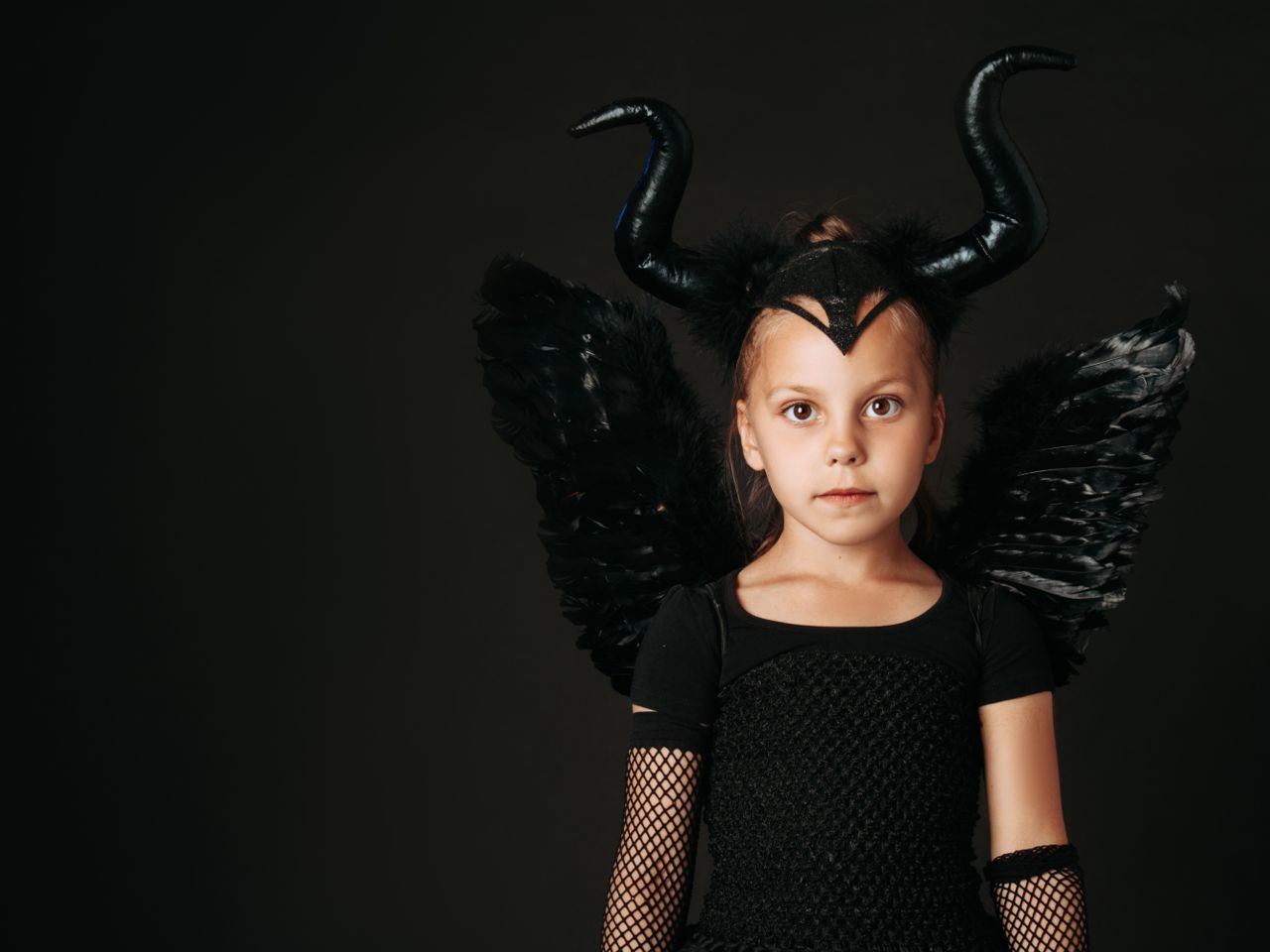 a young girl dressed in a black devil costume with wings and horns on