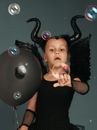 Cute Girl in Devil Costume Pointing at Floating Bubbles