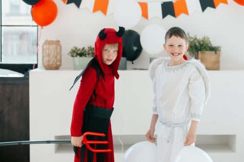 Free Two children dressed as an angel and a devil indoors with Halloween decorations. Stock Photo