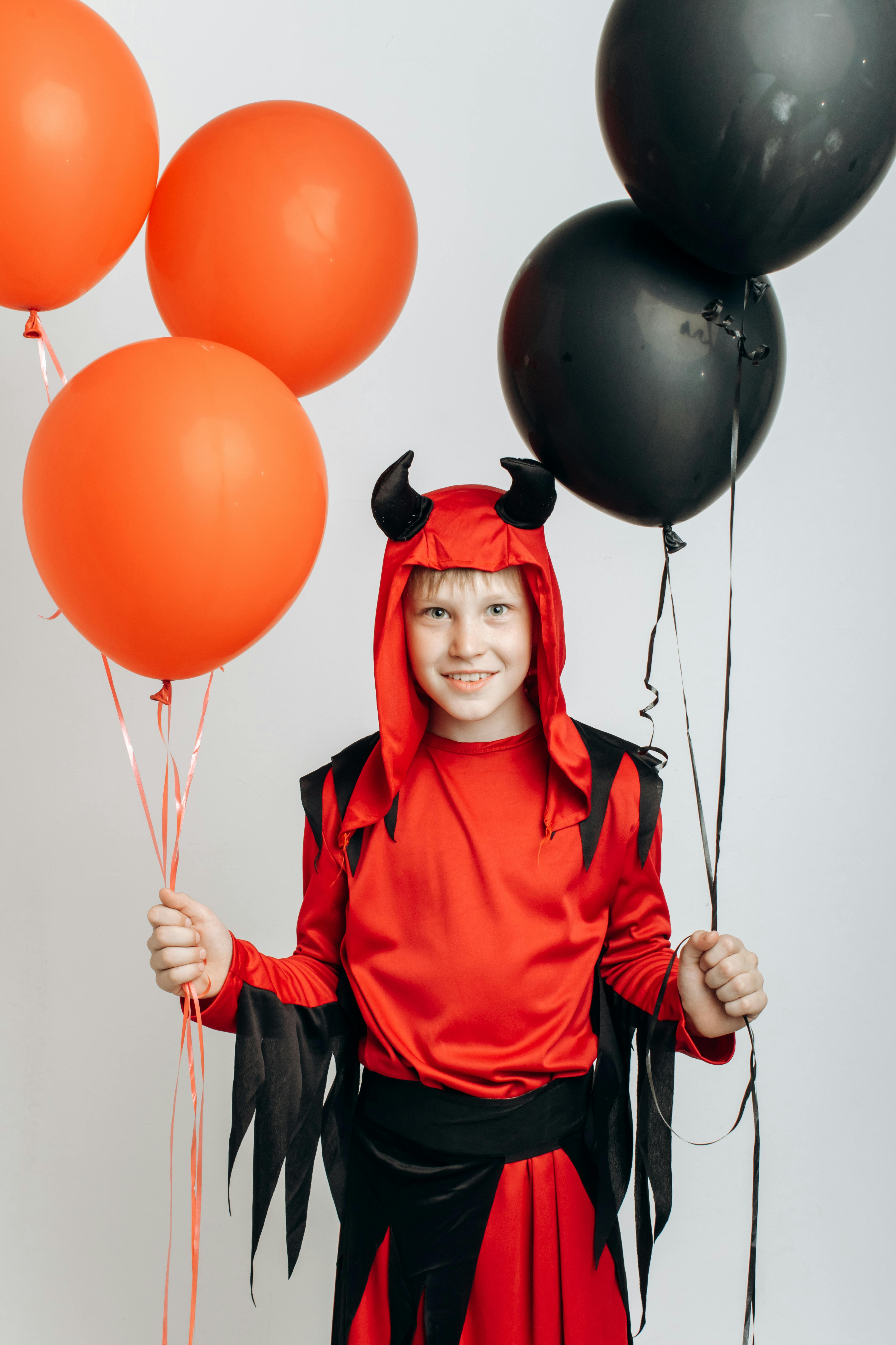 a boy in a devil costume holding balloons