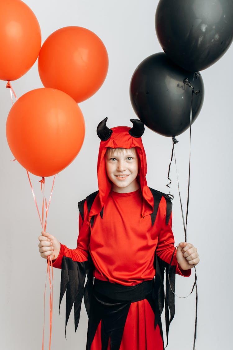 A Boy In A Devil Costume Holding Balloons