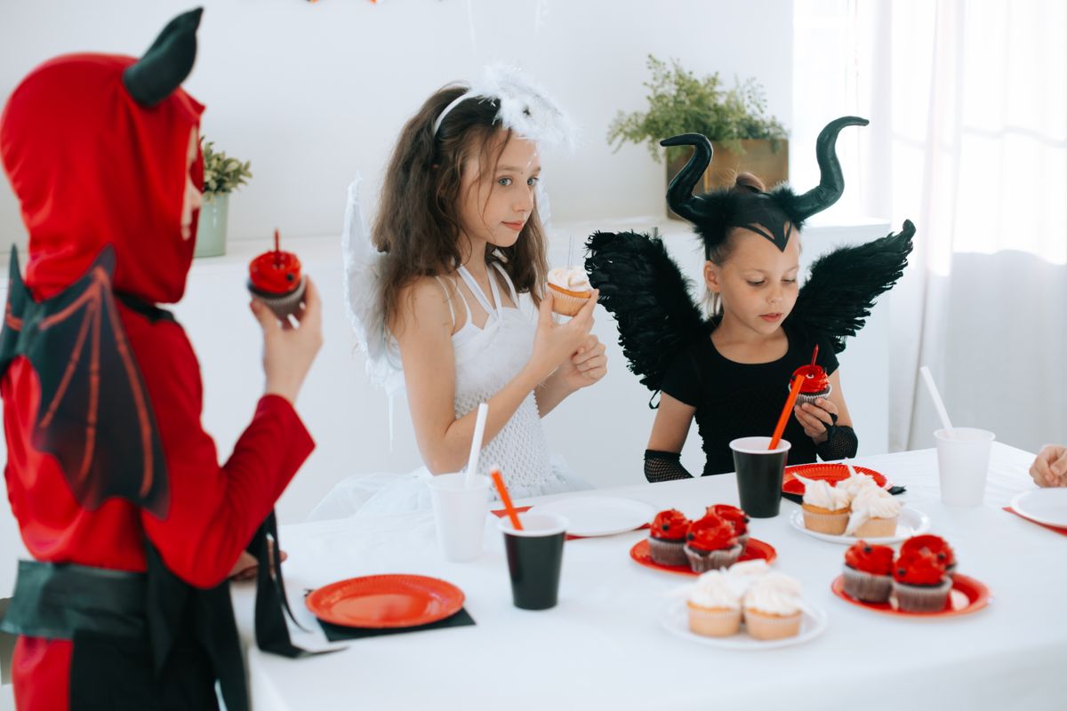 Children in Halloween costumes holding decorated cupcakes.