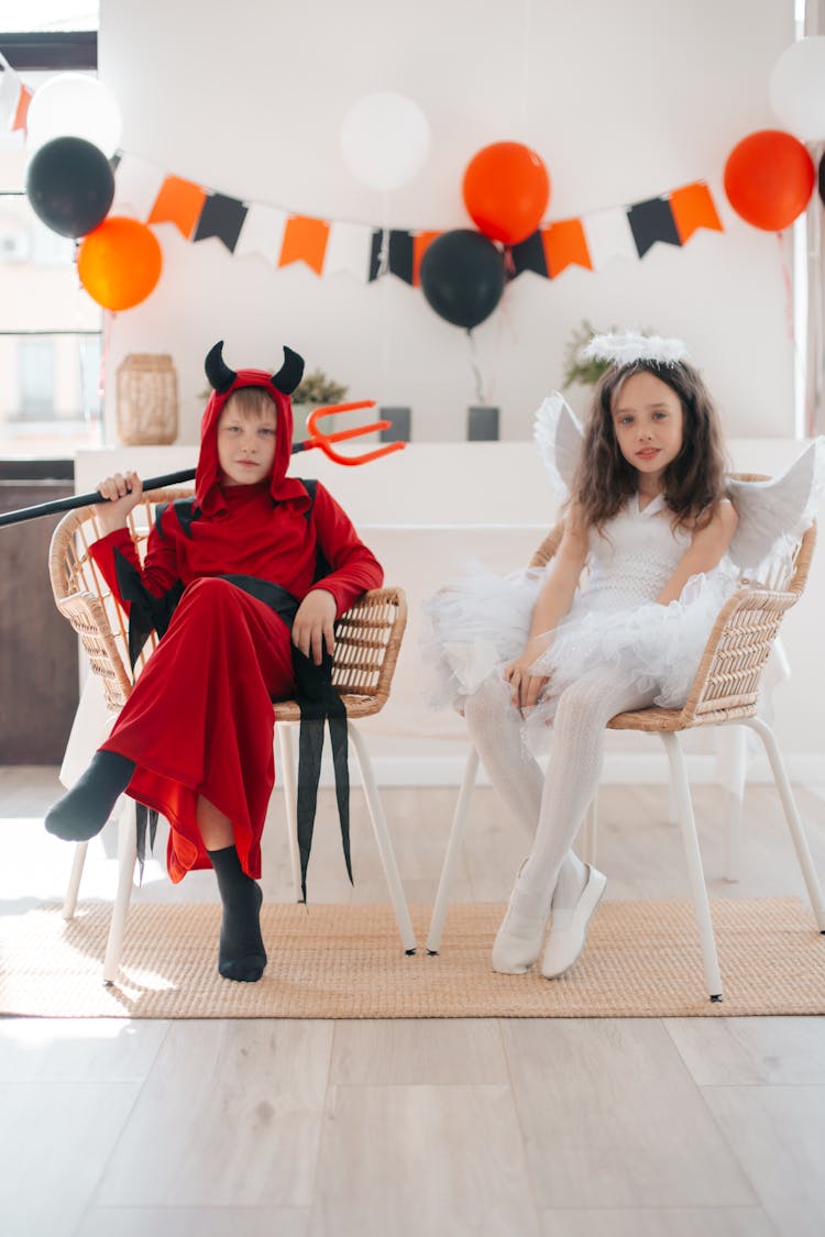 Two Children In Halloween Costumes Sitting On The Chairs