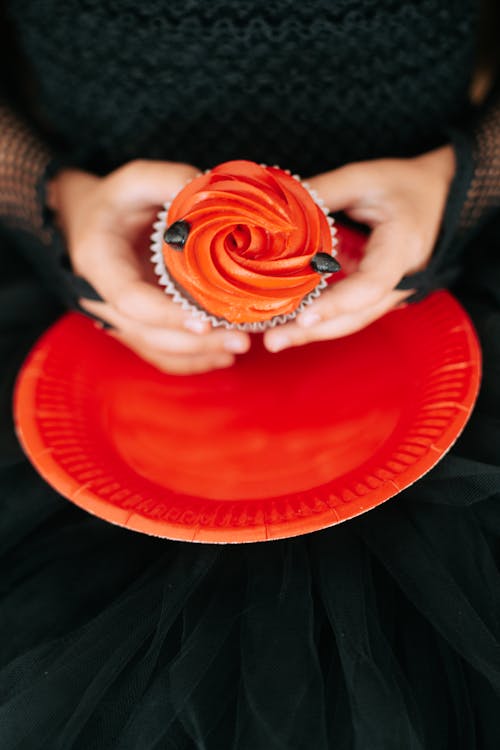 Cupcake with an Orange Cream and Dark Chocolate Held in Childs Hand on an Orange Paper Plate