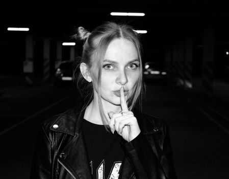 Black and white portrait of a woman making a quiet gesture in an urban garage.