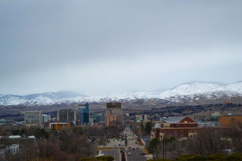 Free Stunning cityscape featuring urban architecture with snow-capped mountains under a cloudy sky. Stock Photo