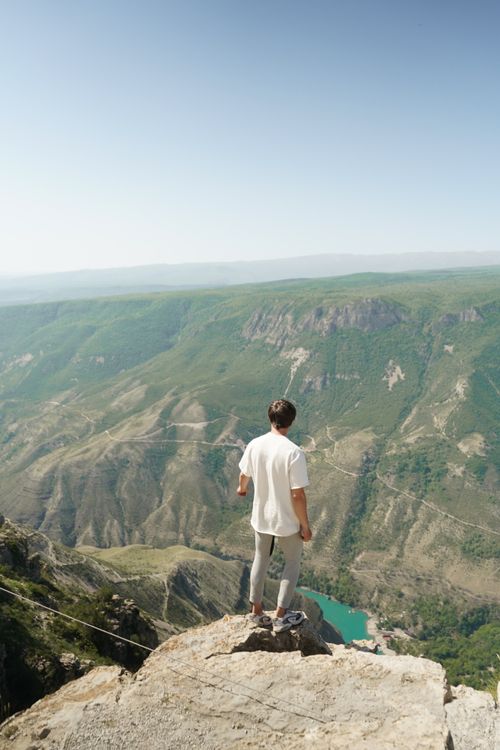 Free A man stands on Dagestan's cliff edge, taking in the breathtaking mountain view. Stock Photo