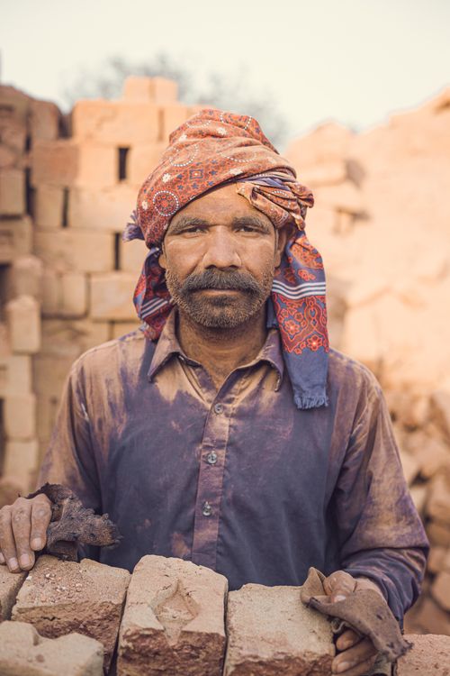 Free A rugged man in traditional attire stands amidst brick stacks, showcasing hard work. Stock Photo