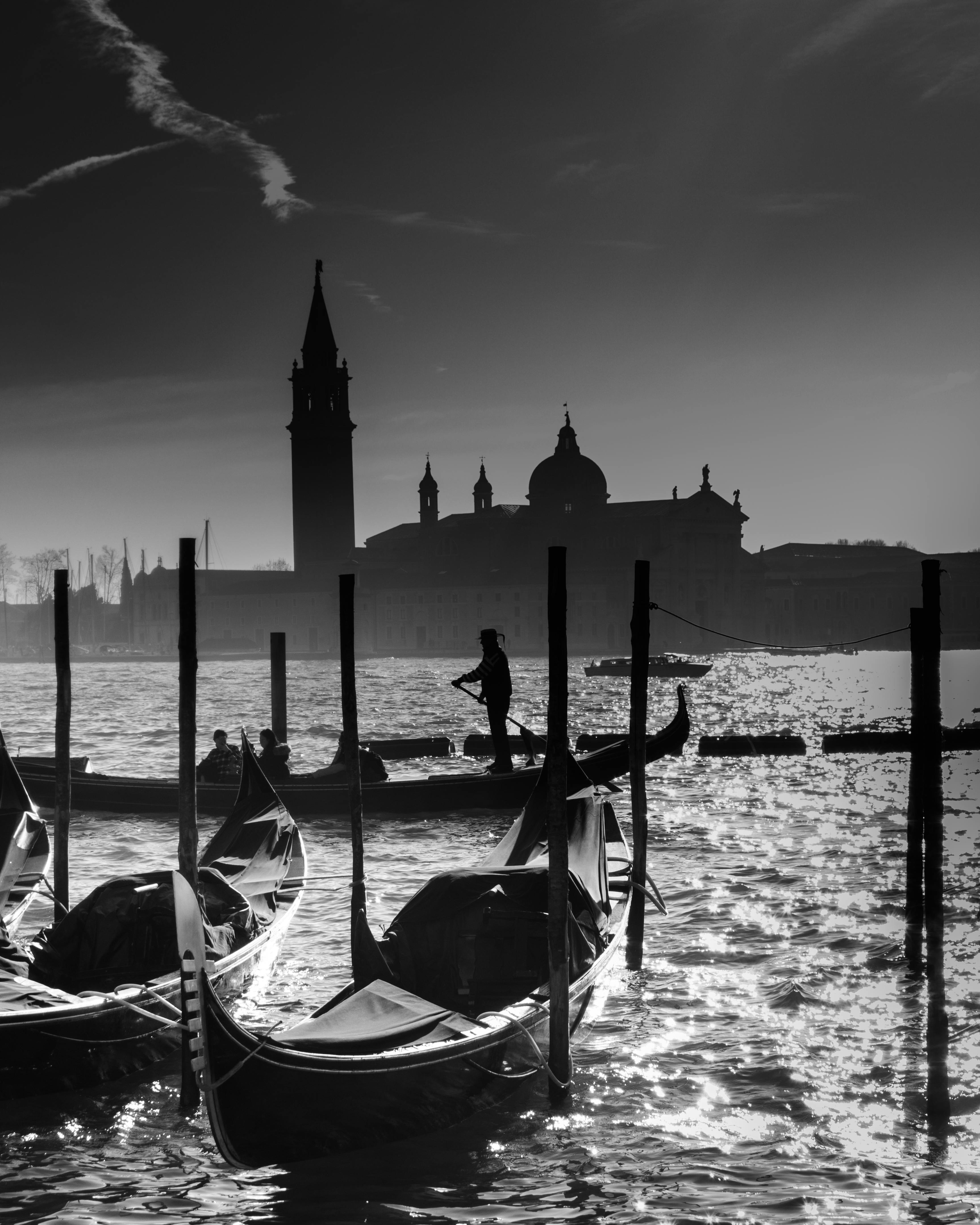 Black and white image of gondolas in Venice with a striking cityscape backdrop.