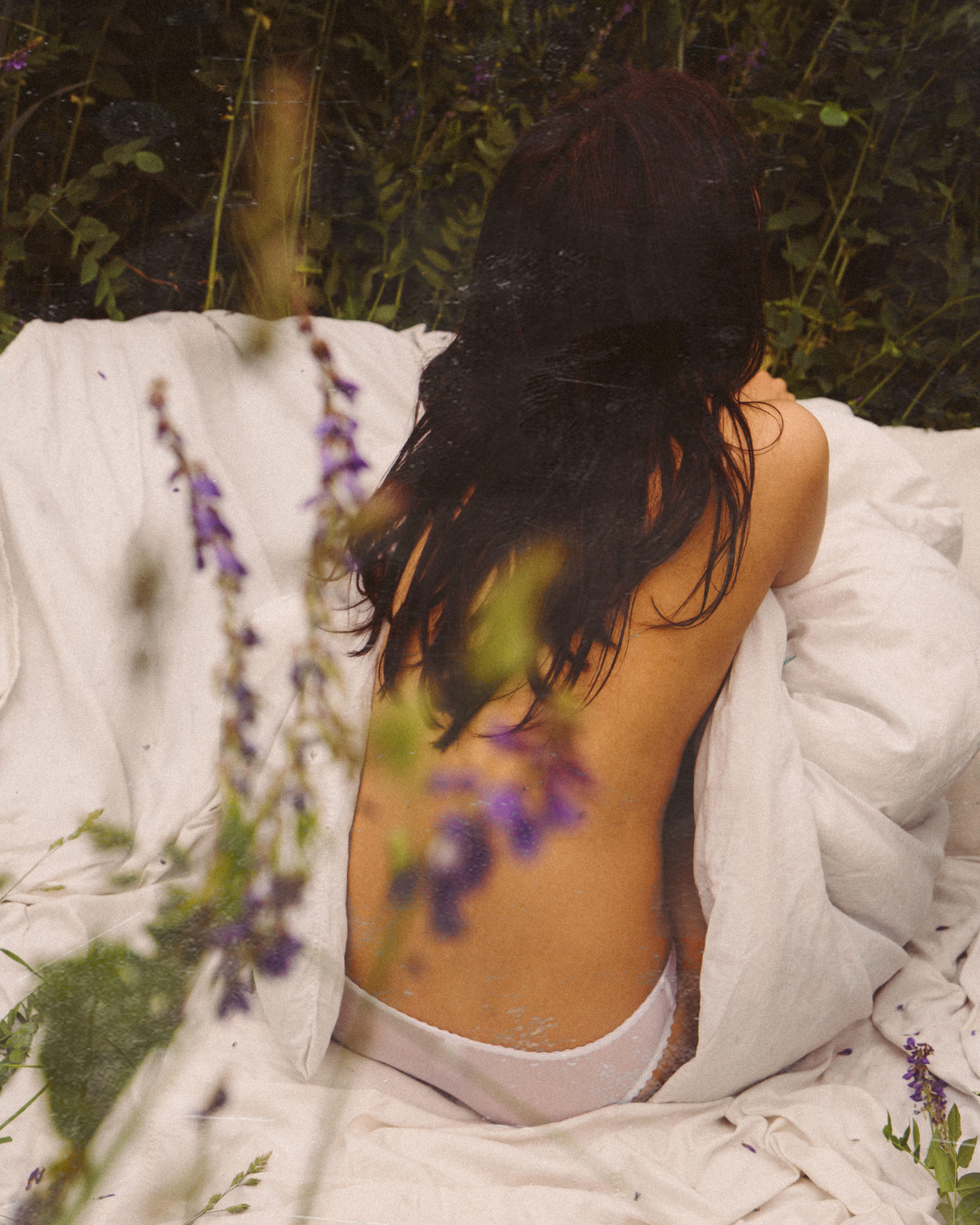 Back view of a woman sitting in nature wrapped in a blanket, exuding tranquility.