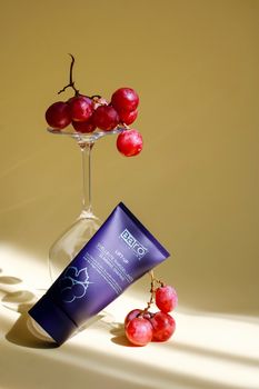 Sophisticated display of skincare tube with grapes in soft lighting, perfect for beauty ads.