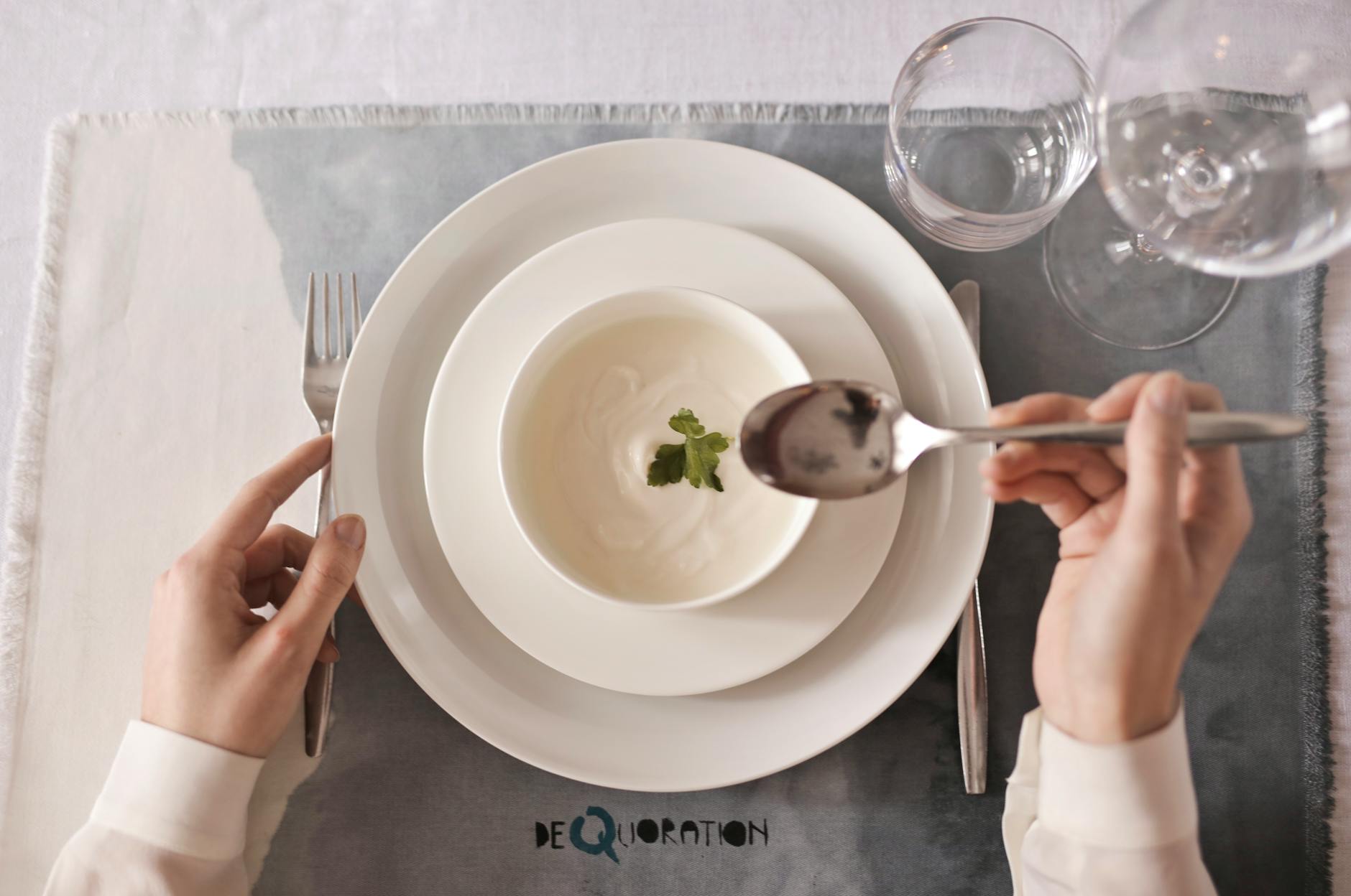 A top-down view of hands ready to enjoy a creamy soup garnished with herbs.