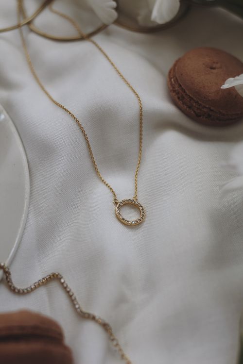 Free Luxurious gold necklace on white silk cloth, accompanied by macarons, creating an elegant scene. Stock Photo
