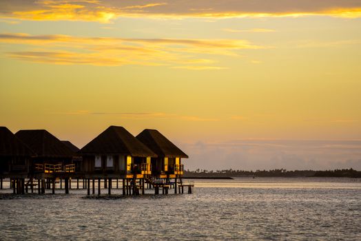 Overwater bungalows against a golden sunset in a tropical paradise. Ideal for travel dreams.