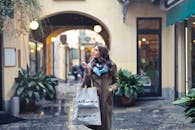 一位时尚女性提着购物袋，走在一条迷人的城市街道小巷里，两旁商店林立