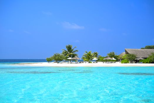 Stunning tropical beach with clear blue water, palm trees, and resort huts, perfect for a relaxing holiday.