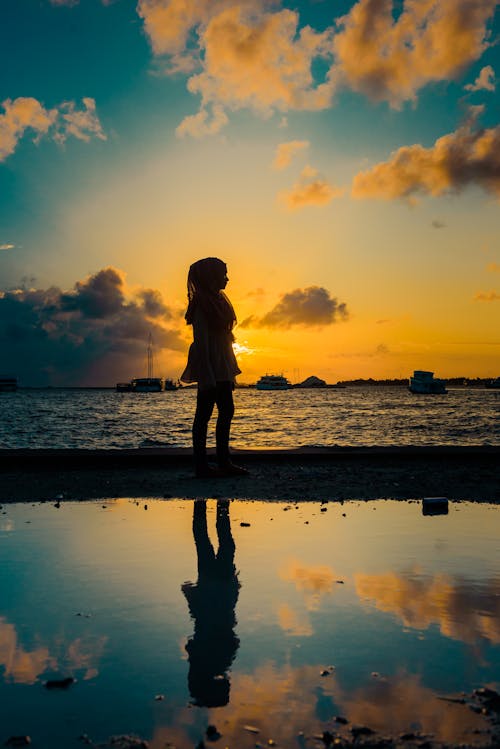 Silhouette of  Woman Near Body of Water During Sunset 