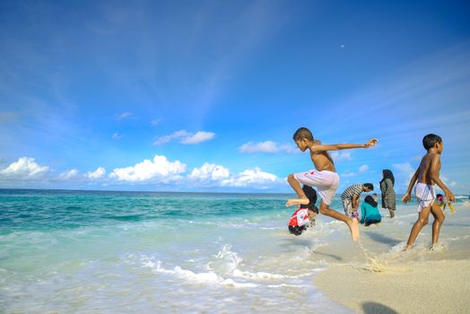 Children enjoying the clear waters and sandy beach in the Maldives, capturing a lively summer moment.