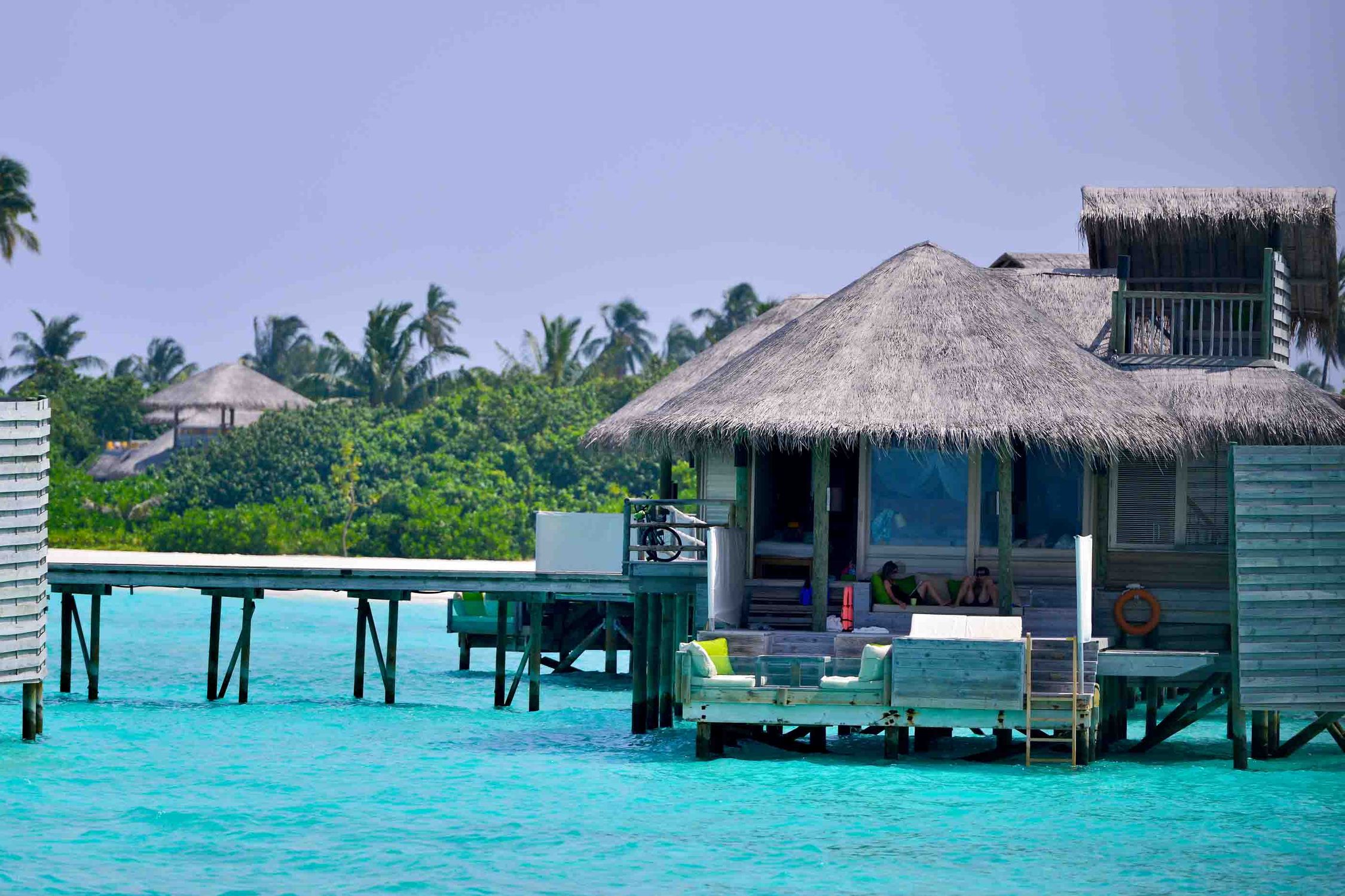 Idyllic overwater bungalow surrounded by turquoise waters and palm trees in the Maldives.