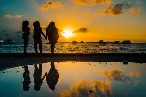 Free Silhouetted figures holding hands by the Maldivian coastline at sunset with ocean reflections. Stock Photo