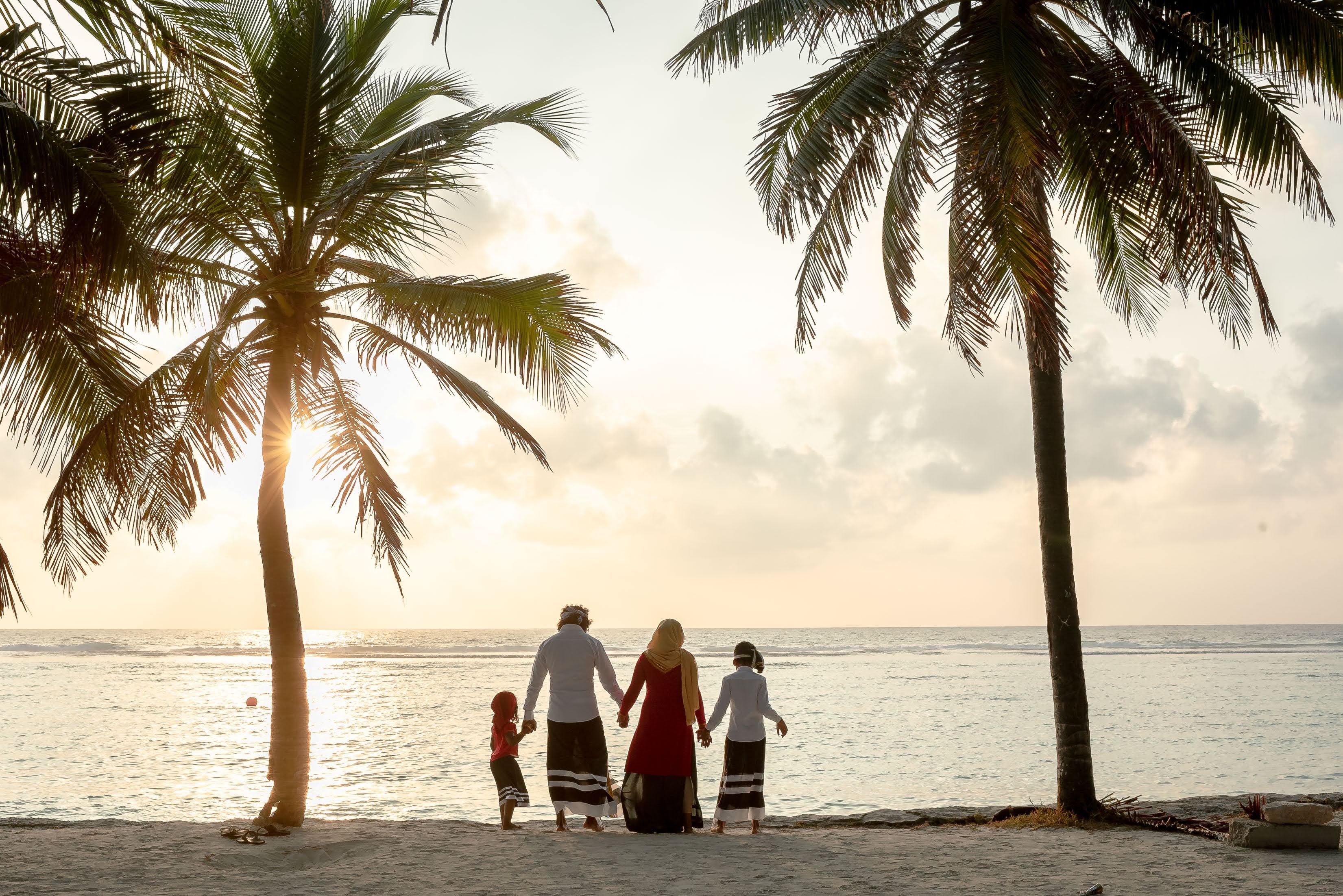 A family holding hands on a tropical beach during sunset, surrounded by palm trees.