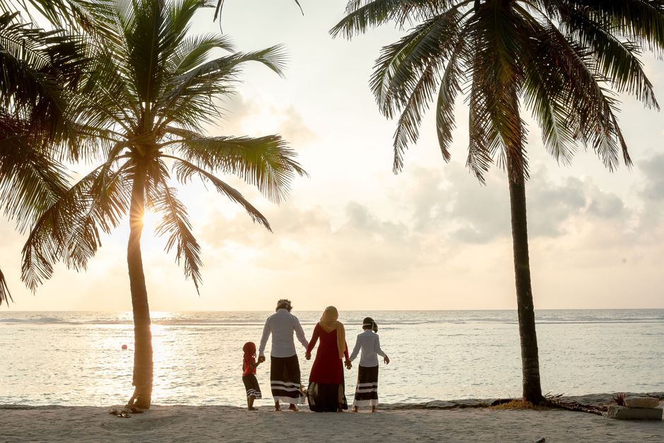 A family holding hands on a tropical beach during sunset, surrounded by palm trees.