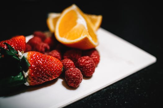 Close-up of strawberries, raspberries, and orange slices on a white surface, highlighting fresh and vibrant colors.