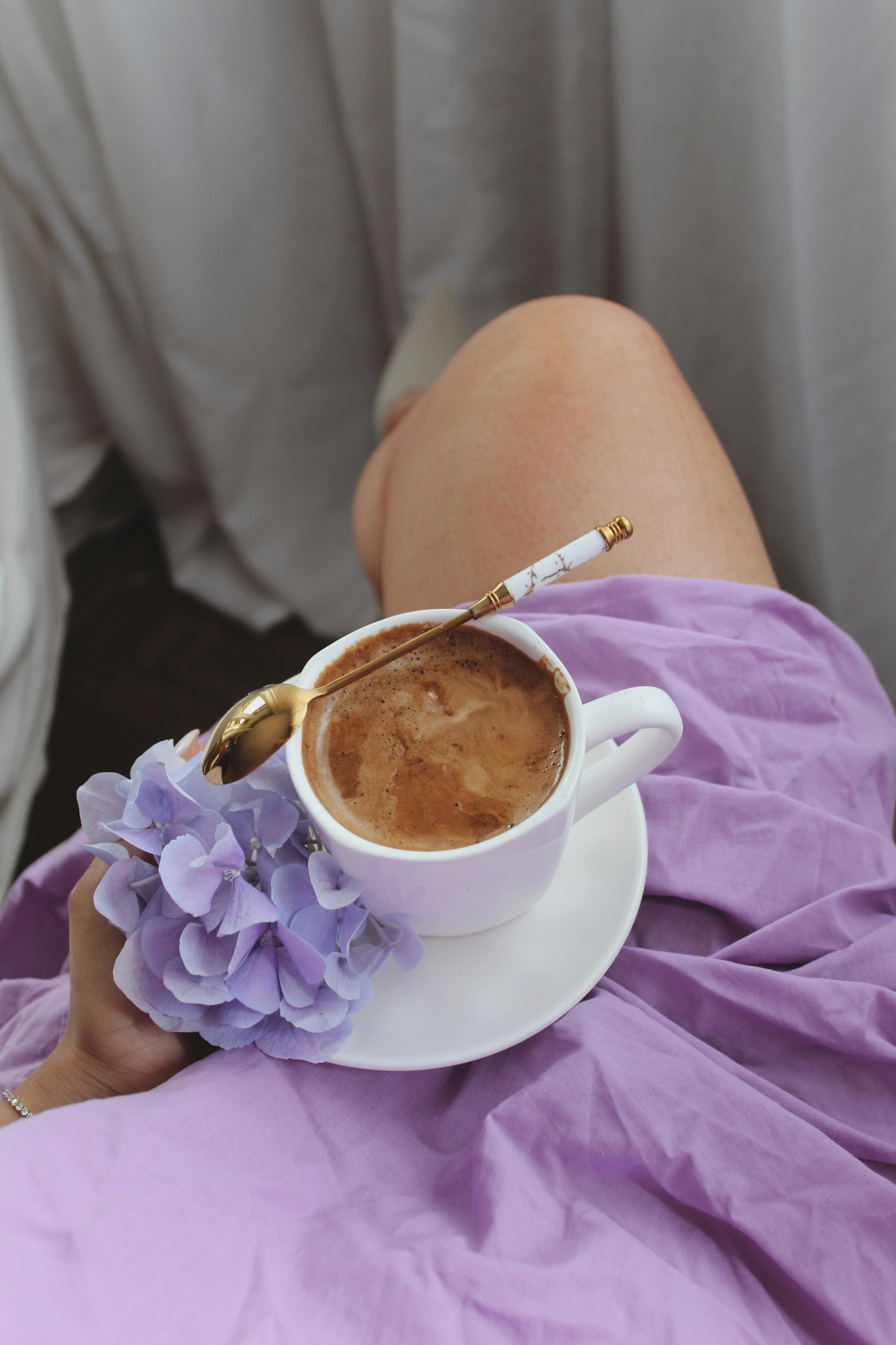 A cozy setting with a woman holding a coffee cup adorned with a purple flower, evoking warmth and relaxation.
