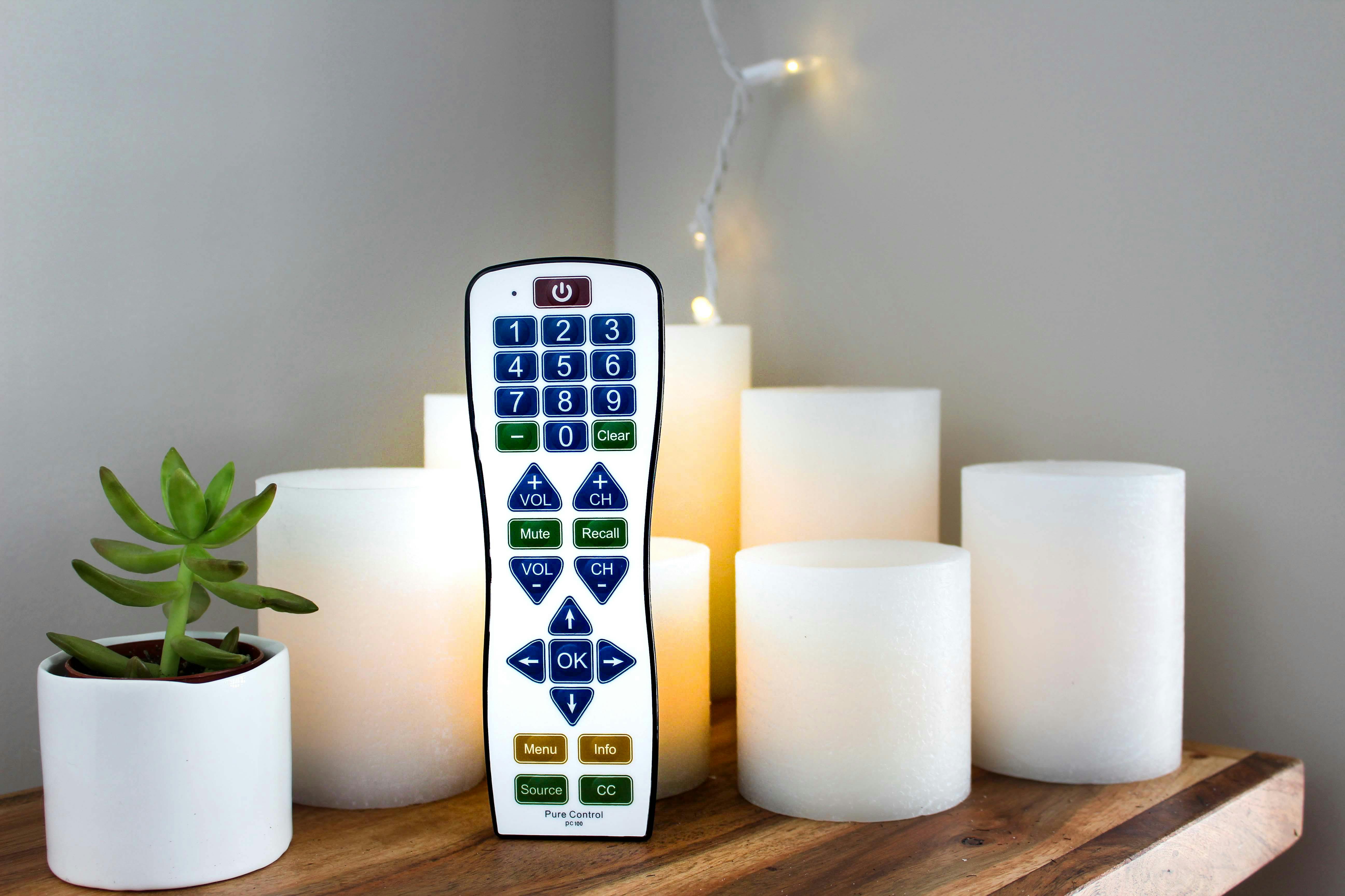 Remote control surrounded by candles and a potted succulent on a wooden tabletop setting.