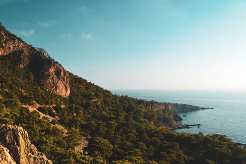 Free Explore a breathtaking coastal landscape featuring lush greenery, mountains, and the serene ocean under a clear blue sky. Stock Photo