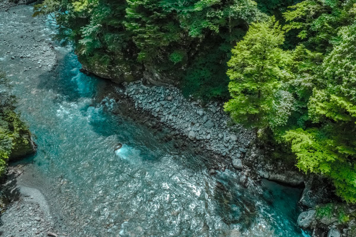 Aerial view of a clear pristine river winding through lush green forested hills in rural Japan