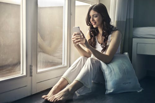 Free Woman Sitting Beside Window Holding Phone Stock Photo