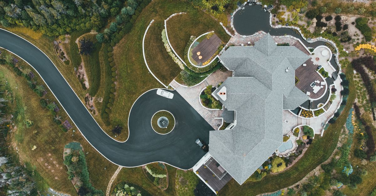 A breathtaking aerial view of a luxury mansion surrounded by a lush landscaped garden and winding driveway.