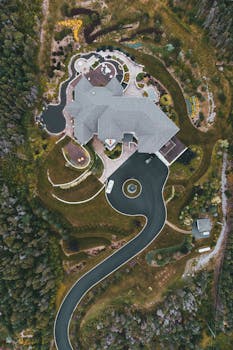 Drone shot of a modern mansion with landscaped gardens and winding driveway.