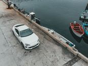A White Car on a Concrete Road Near the Body of Water with Boats