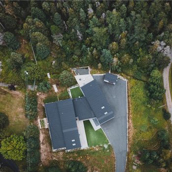 Aerial shot of a modern building surrounded by dense forest greenery.