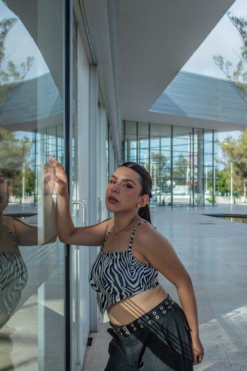 
A Woman Wearing a Crop Top and Black Pants Leaning on the Glass