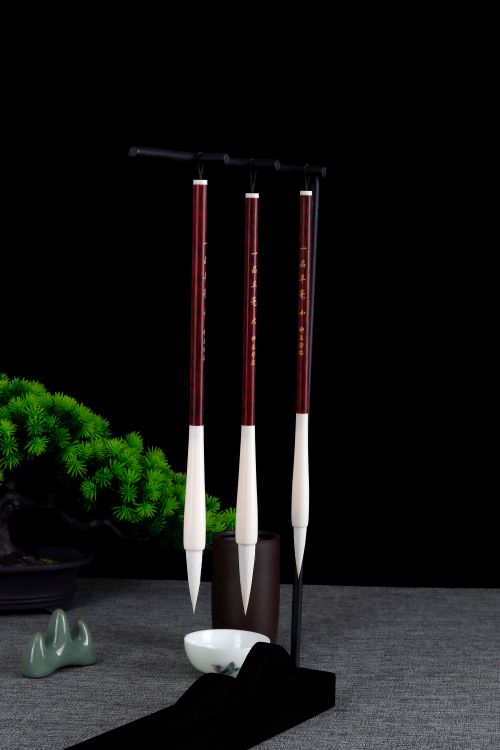 Free A sophisticated set of hanging calligraphy brushes with a bonsai backdrop, perfect for artistic inspiration. Stock Photo