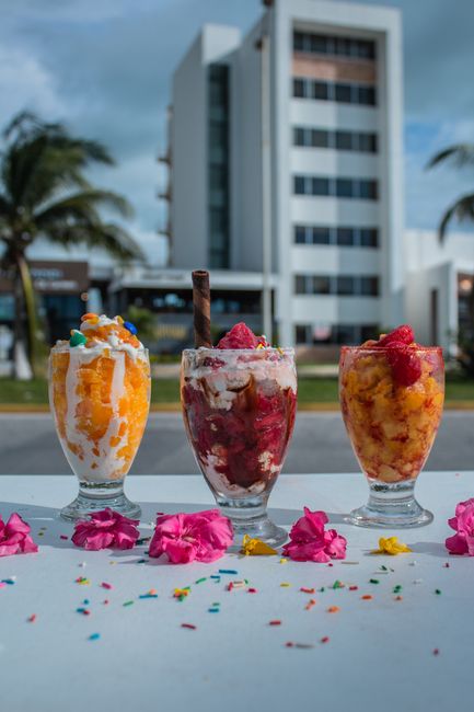 A tall glass of halo halo showing layers of shaved ice, purple ube ice cream, sweet beans, jackfruit, and evaporated milk poured over the top