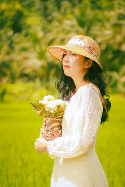 Woman in White Dress and Sun Hat Holding a Vase of Flower