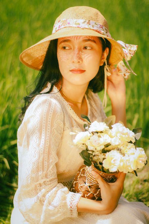 Free Beautiful woman in a sun hat holding white flowers, sitting outdoors in a bright field. Stock Photo