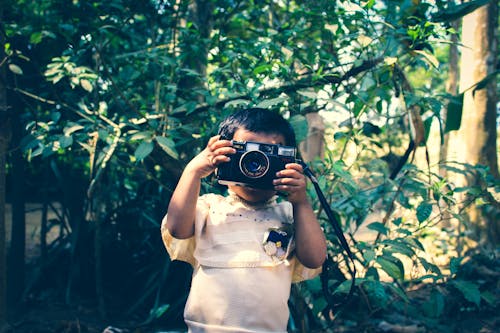Boy Holding Black Flash Camera Near Green Leaf Plants